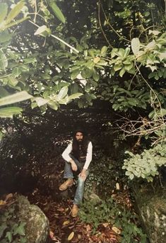 a man with long hair sitting on rocks in the woods next to plants and trees