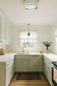 a kitchen with light green cabinets and white counter tops, along with a rug on the floor