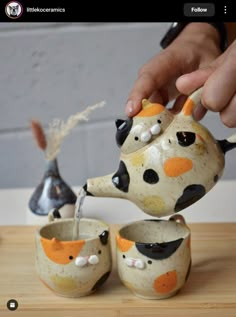 a person is pouring water into three ceramic cups with animals painted on the top and bottom