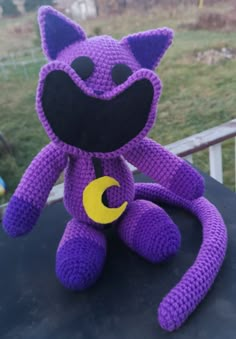 a purple crocheted stuffed animal sitting on top of a black table next to a fence