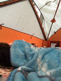 a woman laying in bed under a blue blanket next to an orange and white tent