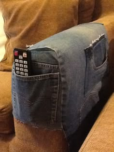 a couch with a remote control in the back pocket and an old pair of jeans on it