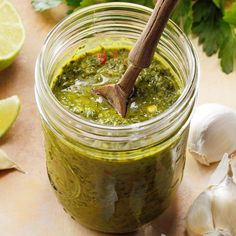 a jar filled with green pesto next to garlic and lime