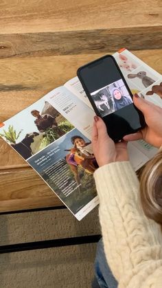 a woman is looking at her cell phone while sitting on the floor next to an open magazine