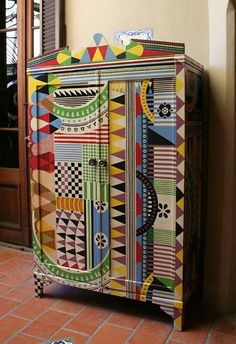 a multicolored painted cabinet sitting in front of a door with an open window