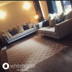 a living room with two couches and a rug on the floor in front of windows