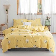 a bed with yellow comforters and pillows in a white room next to a window