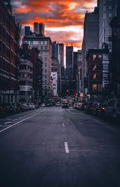 an empty city street with cars parked on both sides and buildings in the background at sunset