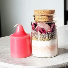 a pink candle sitting next to a glass jar filled with sand and other items on a table