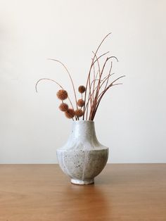 a white vase filled with dry grass on top of a wooden table