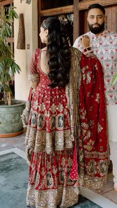 a man standing next to a woman in a red and gold wedding dress with long hair