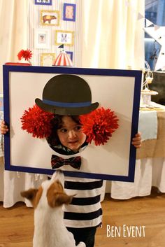 a little boy in a top hat and striped shirt holding up a sign with a dog standing next to him