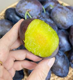 a person holding up a piece of fruit in front of a basket full of plums