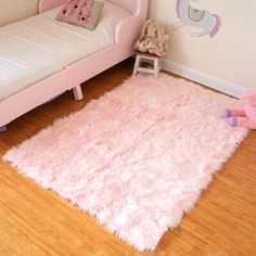 a child's bedroom with a pink bed and white rug on the wooden floor