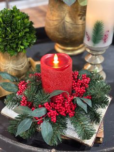 a red candle sitting on top of a table next to some greenery and candles