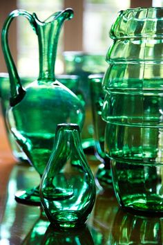 several green glass vases and cups on a table