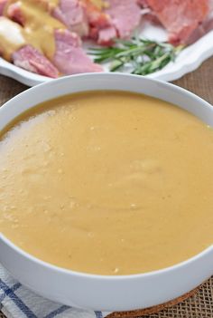 a bowl of soup sitting on top of a table next to a plate of meat