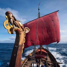 a large red sail boat in the open ocean with people on it's deck