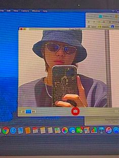 a person wearing sunglasses and a hat holding a cell phone in front of a computer screen