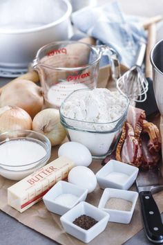 an assortment of ingredients on a cutting board including eggs, meats and flour in bowls