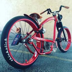 a red bicycle parked in front of a white wall with writing on the tire rims