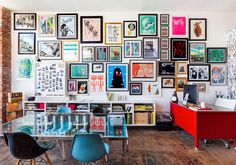 a room with many framed pictures on the wall and chairs in front of a glass table