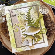 a close up of a card on a wooden table with flowers and plants in the background