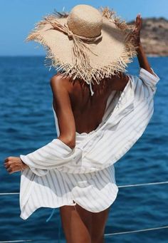 a woman wearing a straw hat standing on the deck of a boat looking out at the ocean