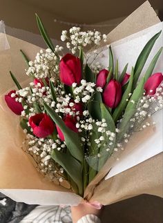 a bouquet of red tulips and white baby's breath in someone's hand