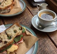 two plates with sandwiches and cups of coffee sitting on a table next to each other