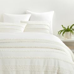 a bed with white comforters and pillows in a room next to a potted plant