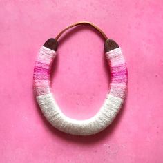 a pink and white bracelet on a pink surface with two wooden beads hanging from it