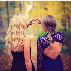 two women standing in the woods making a heart shape with their hands and looking at each other