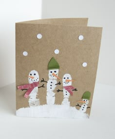 three snowmen with hats and scarves are standing in front of a brown card