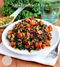 kale fried wild rice on a white plate with silverware and green vegetables in the background