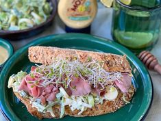 a sandwich with meat, lettuce and sprouts sits on a green plate