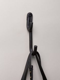 a pair of black scissors hanging from a hook on a white wall in front of a gray background