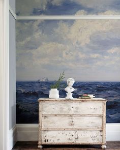 a white dresser sitting in front of a wall with a painting on it's side