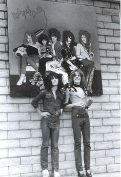 two women standing next to each other in front of a brick wall with an advertisement on it