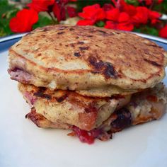 a stack of pancakes sitting on top of a white plate next to red and pink flowers