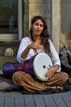 a woman sitting on the ground with a drum in her hand and looking at something