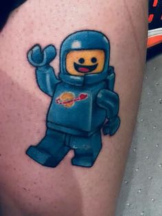 a lego man tattoo on the leg of a person wearing a blue suit and holding his hand up