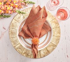 a place setting with napkins and wine glasses on the side, along with flowers