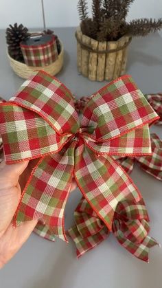 a hand holding a red and green plaid bow on top of a table next to potted plants