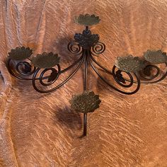 a wrought iron wall mounted candle holder with leaves on the top and bottom, set against a brown velvet background