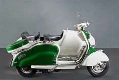 a green and white motor scooter parked in front of a gray wall,