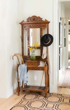 a hat is sitting on top of a wooden bench in front of a mirror and coat rack