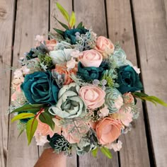 a bridal bouquet is sitting on a wooden table with succulents and greenery