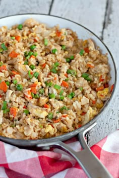 a pan filled with rice and vegetables on top of a red and white checkered table cloth