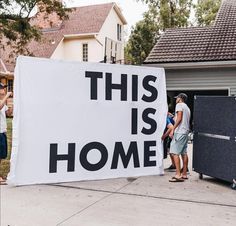 a group of people standing around a sign that says this is home